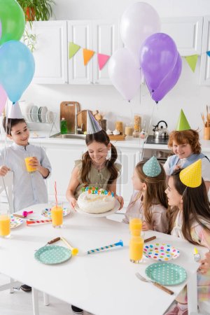 Gruppe fröhlicher Kinder in Partymützen, die sich beim Geburtstag zu Hause vergnügen 