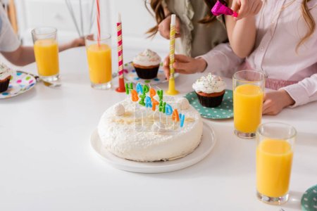 gâteau d'anniversaire fait maison avec des bougies à côté de cupcakes et de verres de jus d'orange 