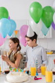 cheerful girl and boy standing near birthday cake with candles next to balloons  Tank Top #650684178