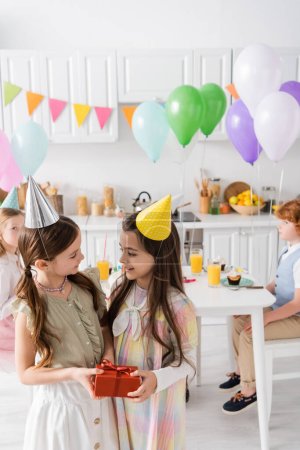 cheerful preteen girl congratulating friend with happy birthday while holding gift box 