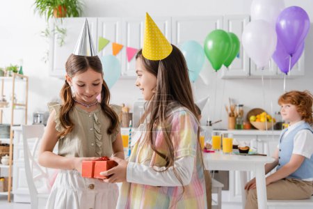 preteen girl congratulating pleased friend with happy birthday while holding gift box 