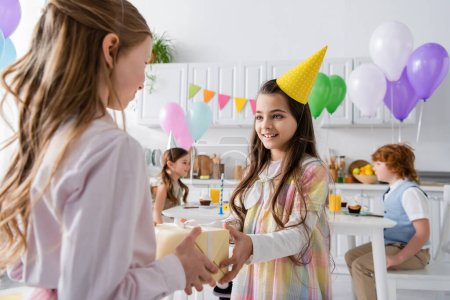 cheerful birthday girl receiving present from friend during birthday party 