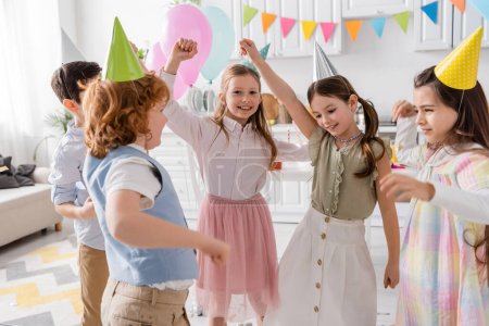 group of happy girls and boys in party caps dancing during birthday celebration at home 