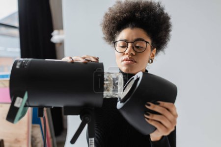 Téléchargez les photos : Afro-américain fabricant de contenu dans les lunettes de montage projecteur stroboscopique dans le studio photo - en image libre de droit
