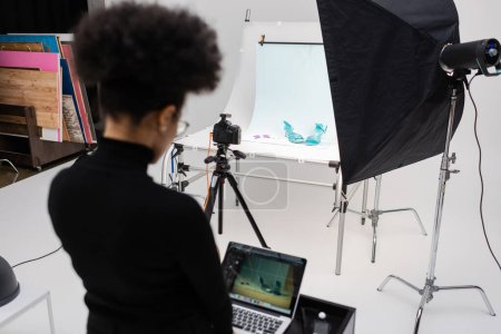 back view of african american content manager working on laptop in photo studio