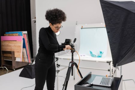 Photo for African american content producer connecting digital camera to laptop in modern photo studio - Royalty Free Image