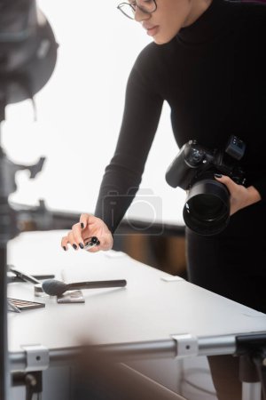 partial view of african american content producer with digital camera and mascara near decorative cosmetics on shooting table in photo studio