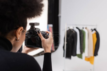 african american content maker photographing blurred collection of clothes in photo studio