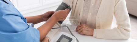 vista recortada de la enfermera multirracial que mide la presión arterial de la mujer mayor, pancarta 