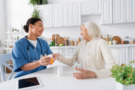 Krankenschwester zeigt skeptischer Seniorin neben digitalem Tablet auf dem Tisch Medikamente 