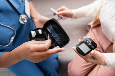 Draufsicht der multirassischen Krankenschwester in Uniform mit Teststreifen in der Nähe einer älteren Frau mit Lanzettstift und Glukometer 