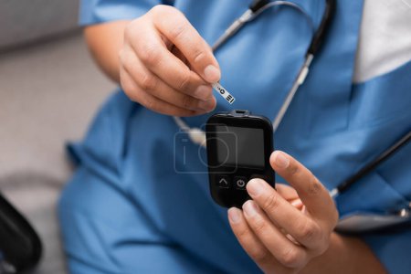 Téléchargez les photos : Vue recadrée de l'infirmière tenant la bande de test et le glucomètre dans les mains - en image libre de droit