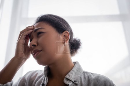 Depressed multiracial woman touching forehead at home 