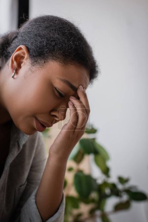 Depressed multiracial woman crying and touching forehead at home 