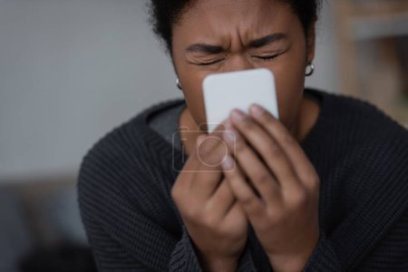 Depressive Frau mit verschwommenem Smartphone zu Hause 