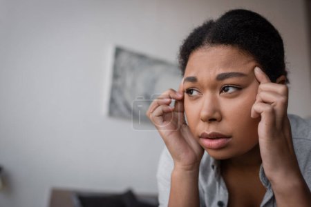 Sad multiracial woman with depression touching head at home 