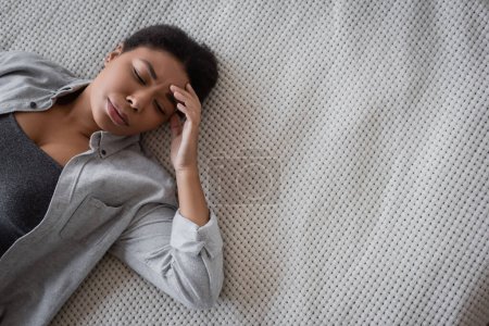 Téléchargez les photos : Vue du dessus de la triste femme multiraciale allongée sur le lit à la maison - en image libre de droit