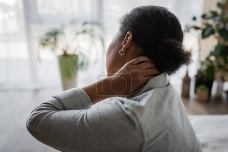 Vue arrière de la femme multiraciale bouclée touchant le cou endolori à la maison 