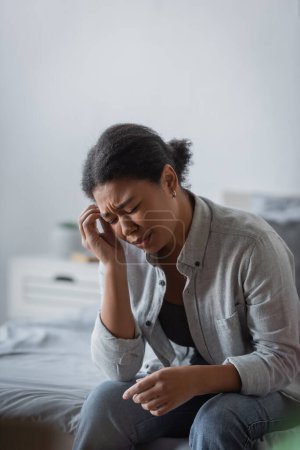 unzufriedene multirassische Frau sitzt mit geschlossenen Augen, während sie Migräne hat 