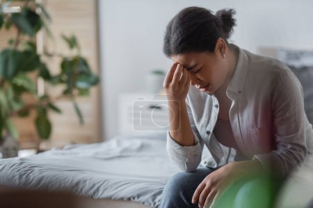Triste mujer multirracial con depresión sentada en la cama en casa 