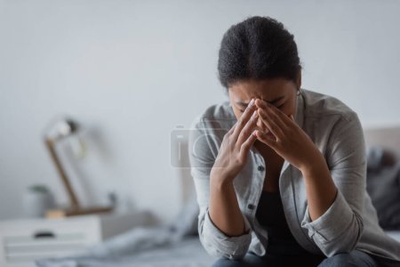 Traurige multirassische Frau berührt Gesicht, während sie im Schlafzimmer weint 