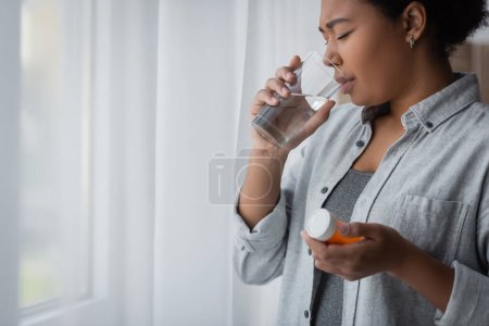 Foto de Mujer multirracial con depresión tomar píldora y beber agua en casa - Imagen libre de derechos