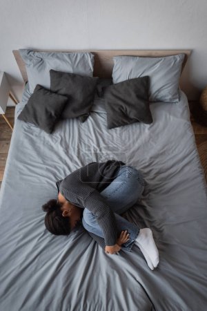 Top view of multiracial woman with depression lying on bed at home 