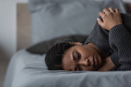 Téléchargez les photos : Femme multiraciale frustrée en pull couché sur le lit à la maison - en image libre de droit