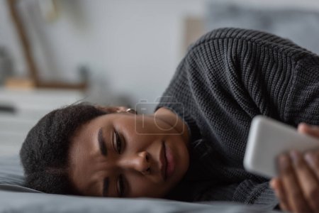Depressive Frau benutzt Mobiltelefon, während sie zu Hause im Bett liegt 