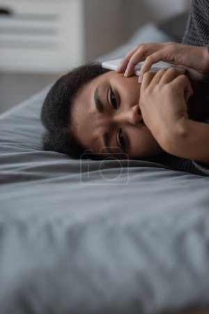 Verärgerte multiethnische Frau spricht auf Smartphone, während sie zu Hause im Bett liegt 