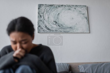 Pintura en la pared cerca de la mujer borrosa multirracial con depresión en el dormitorio 