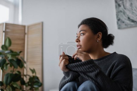 Photo for Sad multiracial woman with apathy touching knitted sweater at home - Royalty Free Image