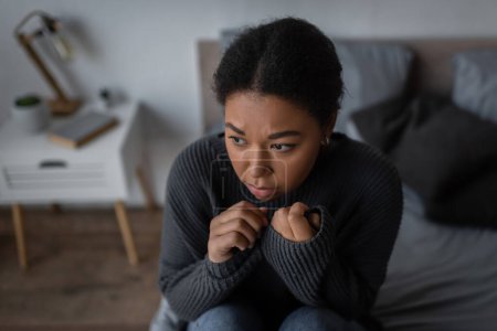 Junge multiethnische Frau mit Depressionen sitzt zu Hause auf verschwommenem Bett