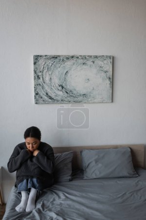 Young multiracial woman with depression sitting on bed at home 