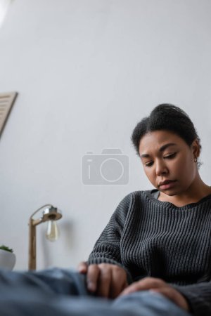 Displeased multiracial woman with apathy sitting in sweater and jeans at home 