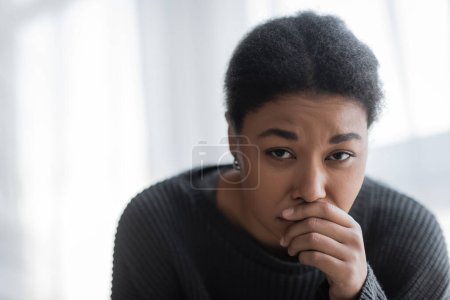 Displeased multiracial woman in knitted sweater looking at camera at home 