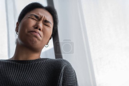 Tiefer Blickwinkel auf junge multiethnische Frau mit Depressionen, die zu Hause weint 