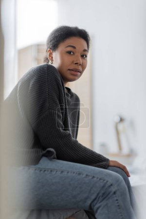 Foto de Mujer multirracial estresada con problemas mentales mirando a la cámara en el dormitorio borroso en casa - Imagen libre de derechos
