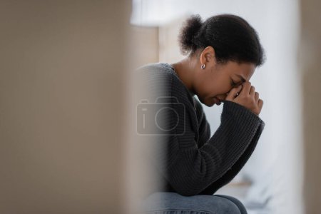 Téléchargez les photos : Vue latérale de la femme multiraciale avec un problème mental pleurer à la maison - en image libre de droit