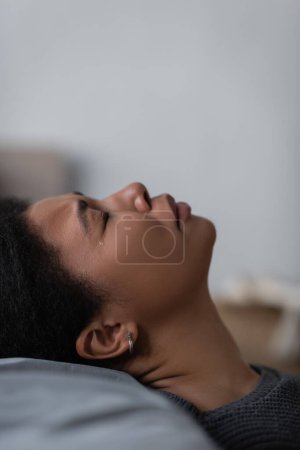 Photo for Side view of heartbroken multiracial woman crying on pillow at home - Royalty Free Image