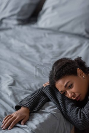 Téléchargez les photos : Jeune femme multiraciale avec apathie assise près du lit à la maison - en image libre de droit