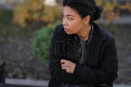 Young multiracial woman with depression sitting outdoors in autumn 