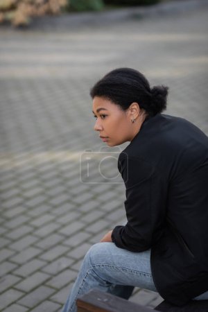 Junge multiethnische Frau mit psychischen Problemen sitzt auf Bank im Freien 