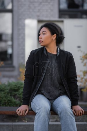 Photo for Multiracial woman with apathy looking away while sitting on bench on urban street - Royalty Free Image