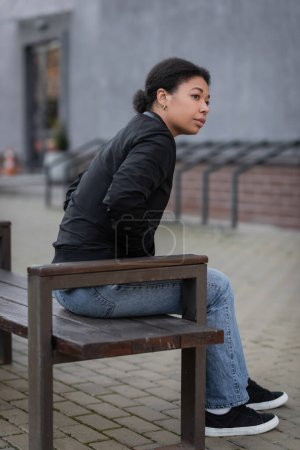 multiracial woman with mental crisis sitting on bench on urban street 