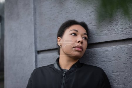 Unzufriedene multirassische Frau mit psychischen Problemen steht in der Nähe einer Mauer im Freien 