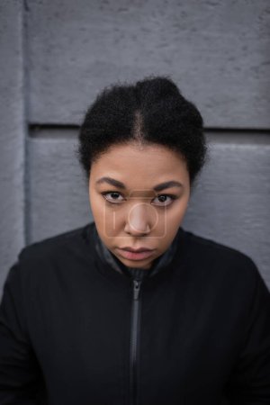 Porträt einer multirassischen Frau mit psychischen Problemen, die in der Nähe von Gebäuden im Freien in die Kamera schaut 