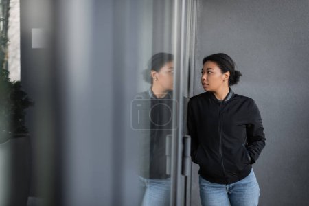 Photo for Multiracial woman with depression looking at glass on door of building outdoors - Royalty Free Image
