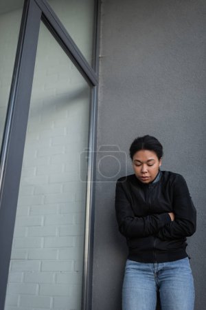 Junge multiethnische Frau mit Apathie steht in der Nähe von Gebäuden im Freien 