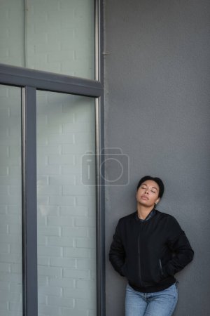 Vielrassige Frau mit Depressionen hält Hände in Taschen in der Nähe von Gebäuden im Freien 